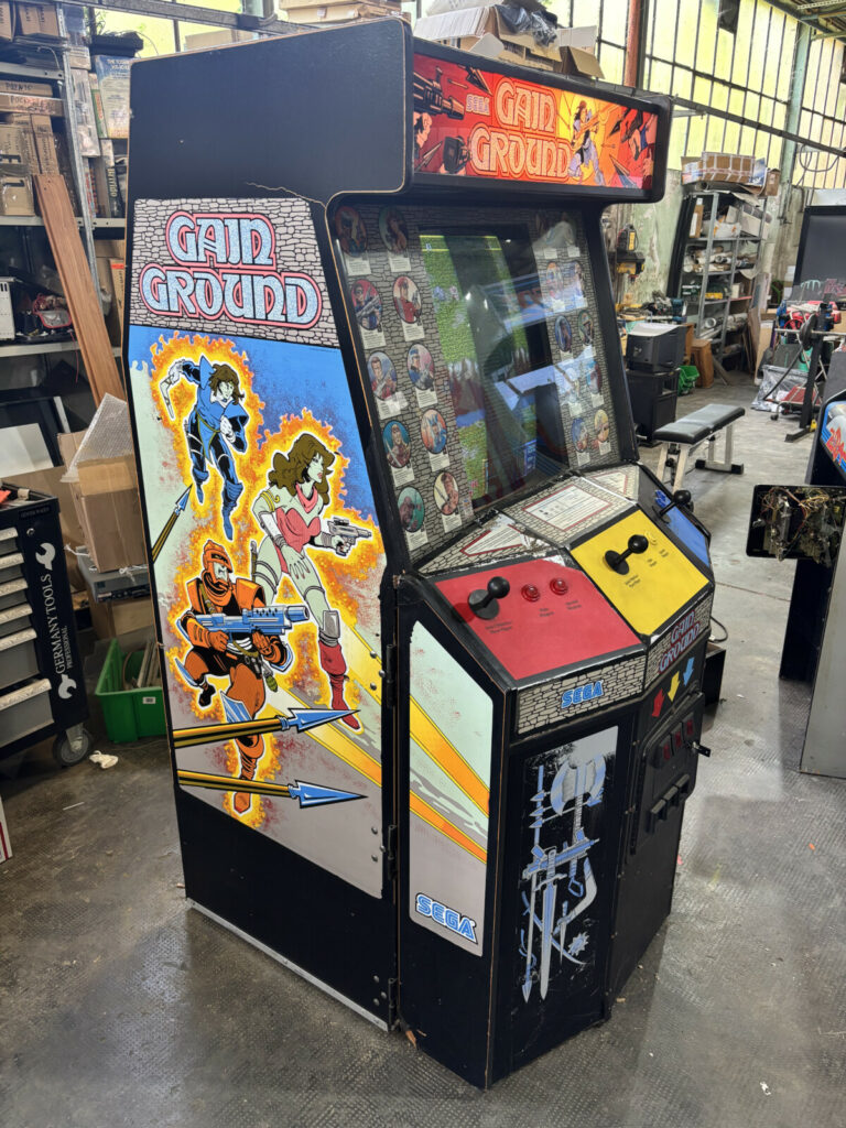 Profilo sinistro del mobile da sala giochi Gain Ground della SEGA, in evidenza il design della versione dedicata a tre postazioni