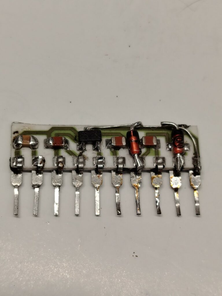 Fotografia macro di un componente elettronico custom TRJ-001 estratto da una scheda arcade. L'involucro di plastica esterna è stato rimosso chimicamente nel laboratorio Arcade Story per esporre e riparare i contatti interni bruciati, salvando la PCB originale